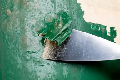 Metal scraper removing green paint from surface
