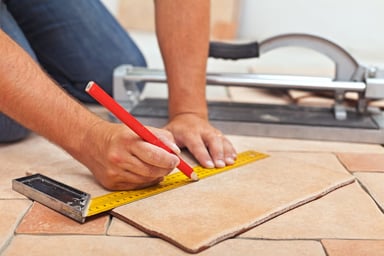 Person measuring and marking a tile with a ruler and pencil